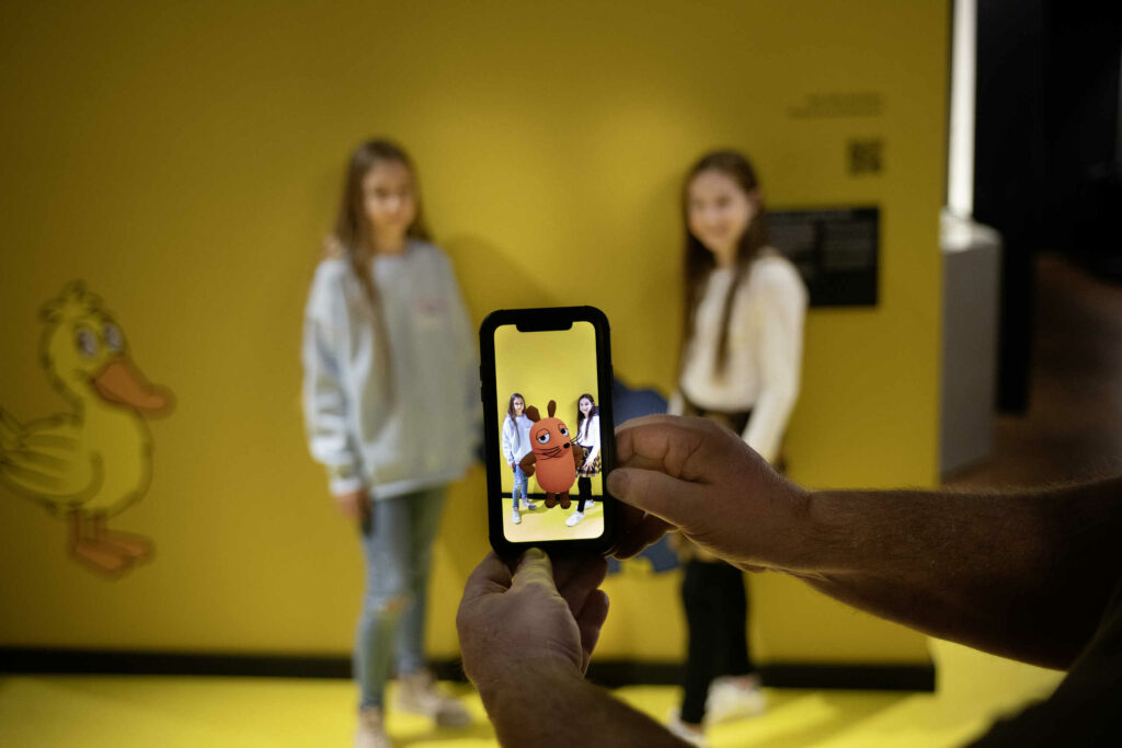 Zwei Kinder werden mit dem Smartphone fotografiert. Auf dem Screen sind die Kinder zusammen mit einer virtuell hinzugefügten Maus zu sehen.