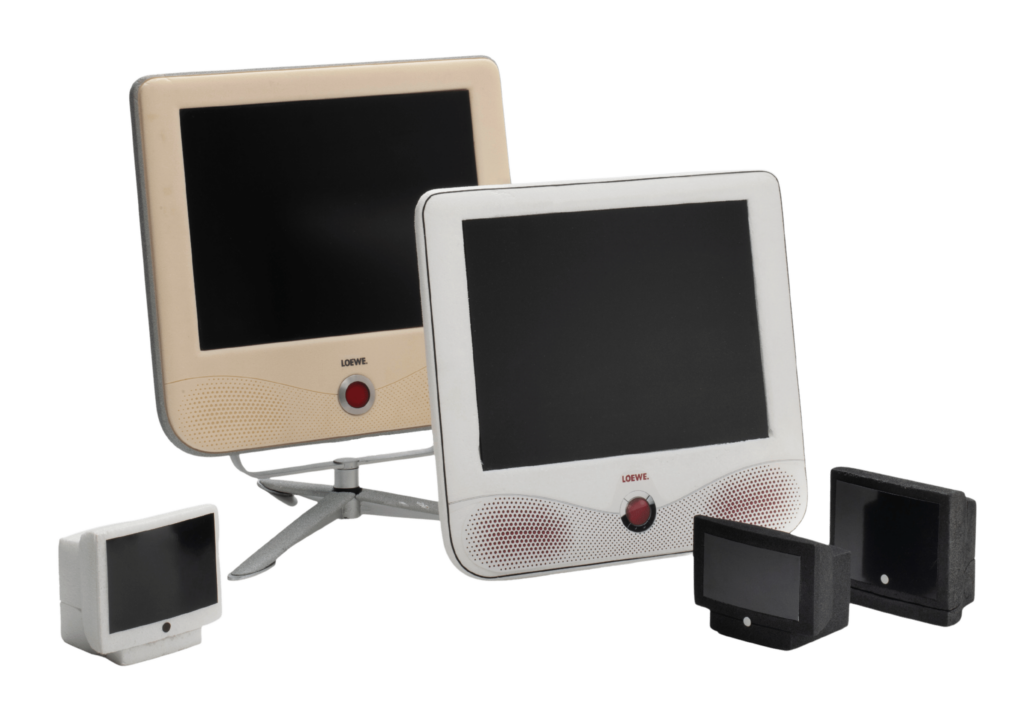 Zu sehen sind mehrere Fernsehgeräte der Firma Loewe, darunter schwarze Röhrenfernseher und zwei Flachbildfernseher in weiß und beige.
